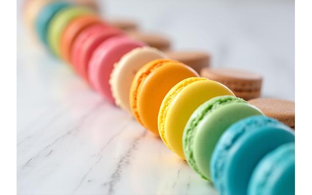 Une série de macarons colorés et parfaitement formés alignés sur un comptoir de cuisine, reflétant la lumière.